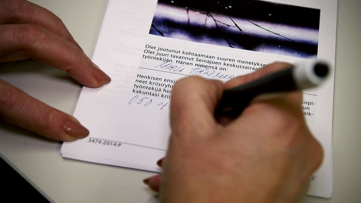 Mirja Fältmars kirjaa lappua, joka annetaan henkisen ensiavun tapaamisessa asiakkaalle tai potilaalle.
