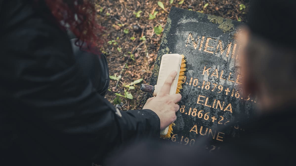 Nainen ja mies pesevät vanhaa hautakiveä