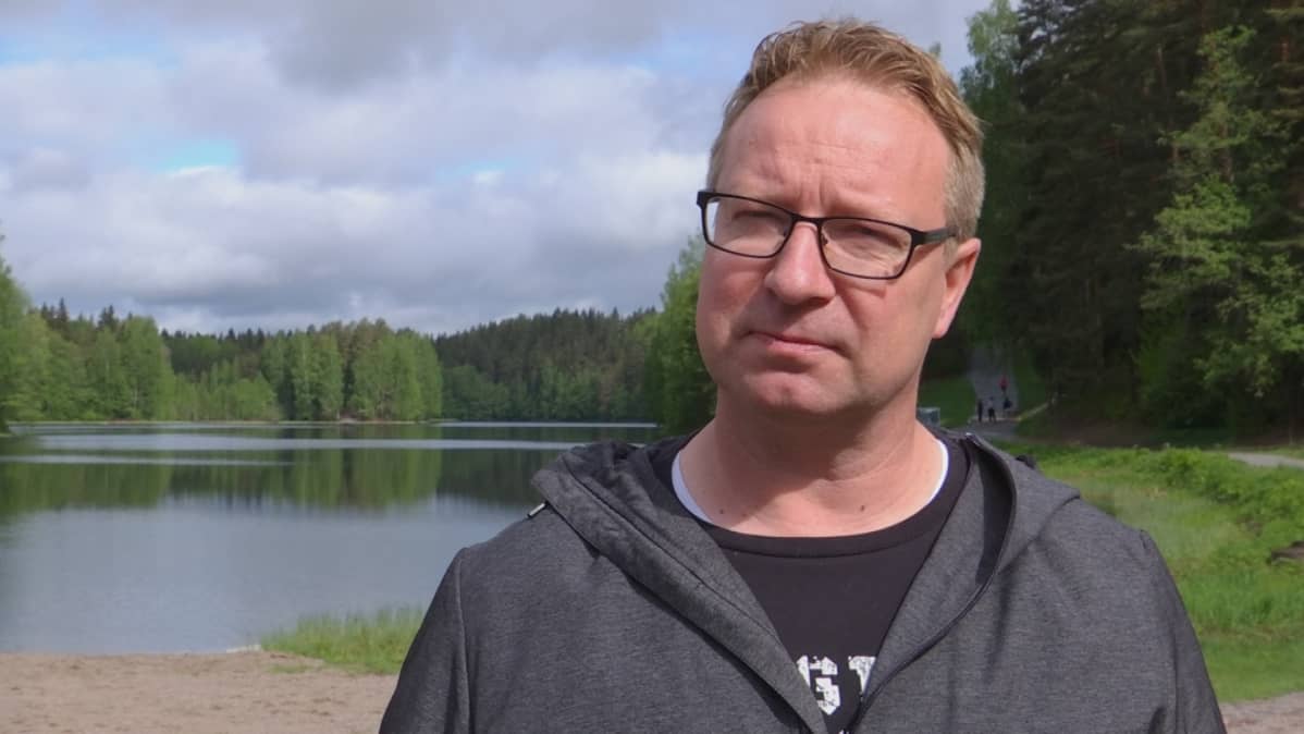 Mies seisoo järven rannassa ja katsoo kameraan.