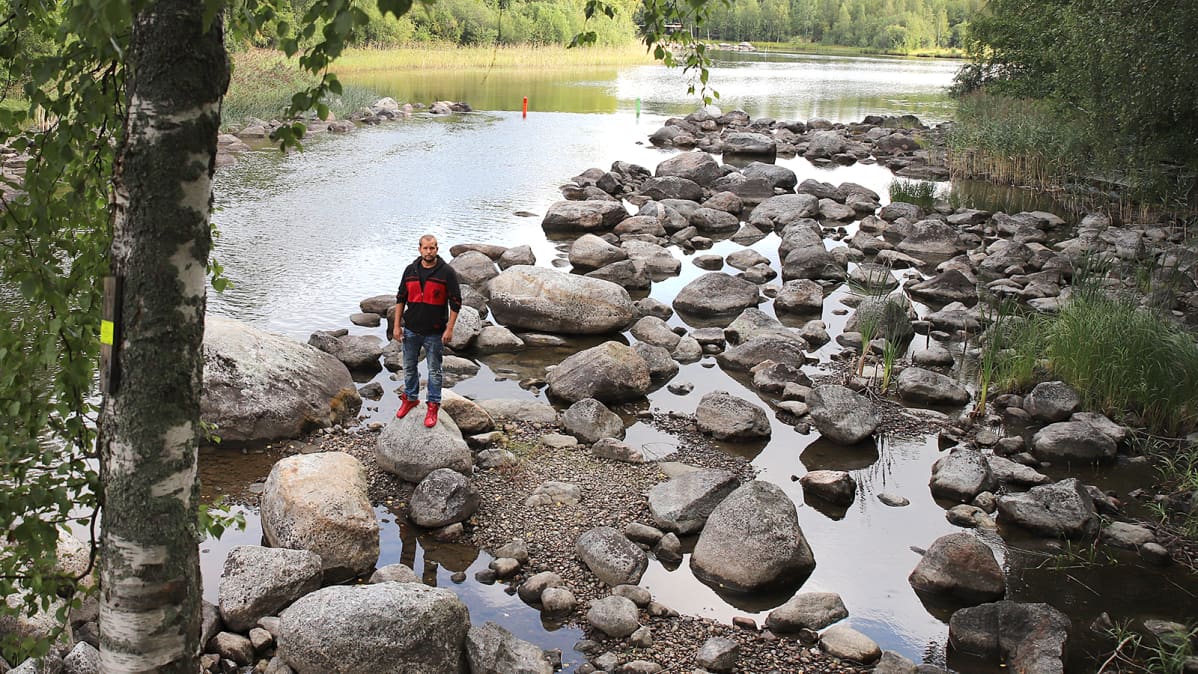 Mies seisoo vedenvähyydestä kärsivän virran kuivilla kivillä