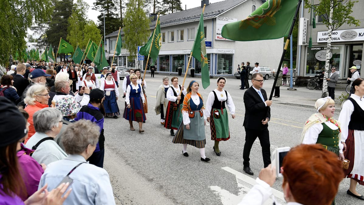 Pääjuhlan lippumarssi Sotkamon keskustassa, kärjessä varapuheenjohtaja Juha Rehula, seuraavana perhe- ja peruspalveluministeri Annika Saarikko ja puoluesihteeri Riikka Pirkkalainen, joita seuraa puolueen puheenjohtaja pääministeri Juha Sipilä sekä varapuheenjohtajat Hannakaisa Heikkinen ja Katri Kulmuni keskustan puoluekokouksessa Sotkamossa sunnuntaina 10. kesäkuuta 2018.
