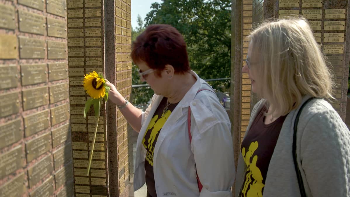 Helena Leinonen ja Maj-Lis Dahl jättävät auringonkukan Renegades-laulajan Kim Brownin haudalle (uurnalehdon muistopaasi) Hietaniemen hautausmaalla Helsingissä 1.8. 2019.