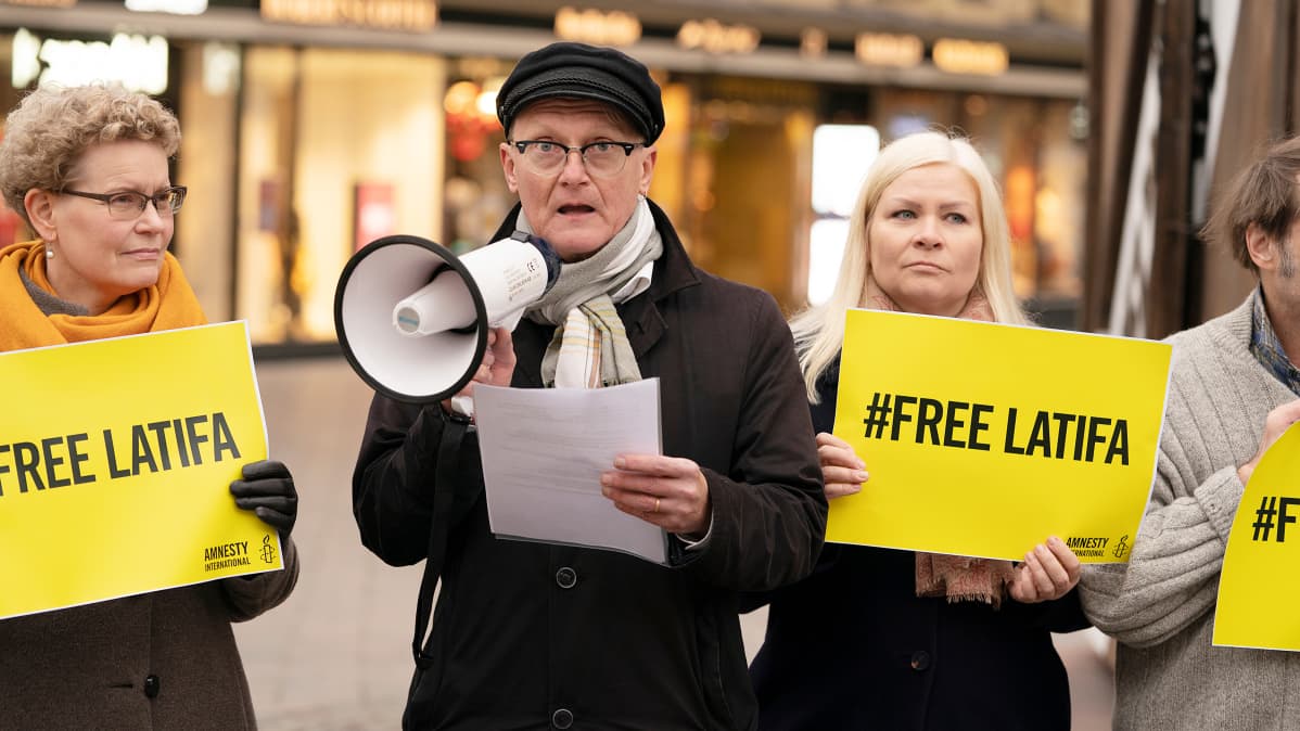Amnesty Internationalin Suomen osaston toiminnanjohtaja Frank Johansson megafoni kädessään. Vieressä Tiina Jauhiainen ja muita mielenosoittajia.
