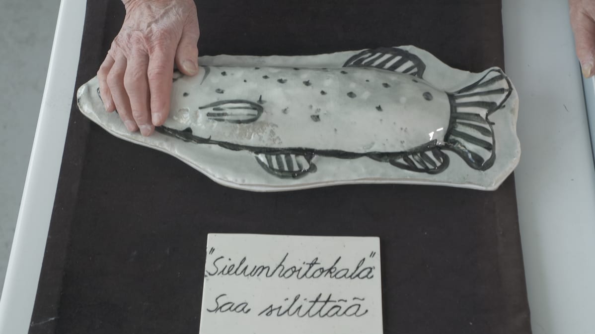 Vanhan naisen käsi silittää keraamista "sielunhoitokalaa."