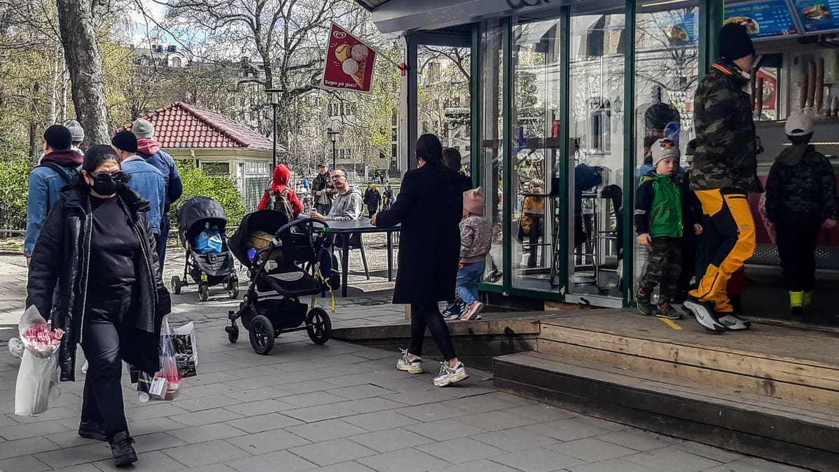 Ihmiset juovat kahvia ulkona ja asioivat kioskilla.
