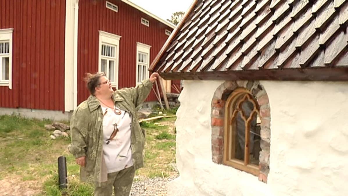Kuvassa Leena Harjunpää tutkii rakennuttamansa Suomen pienimmän kivikirkon paanukattoa