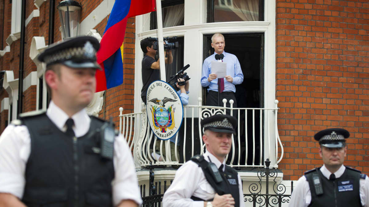 Julian Assange puhuu Ecuadorin Lontoon-suurlähetystön parvekkeella, etualalla poliiseja.