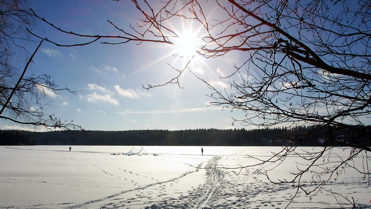 Aurinko paistaa järveen jään yllä.