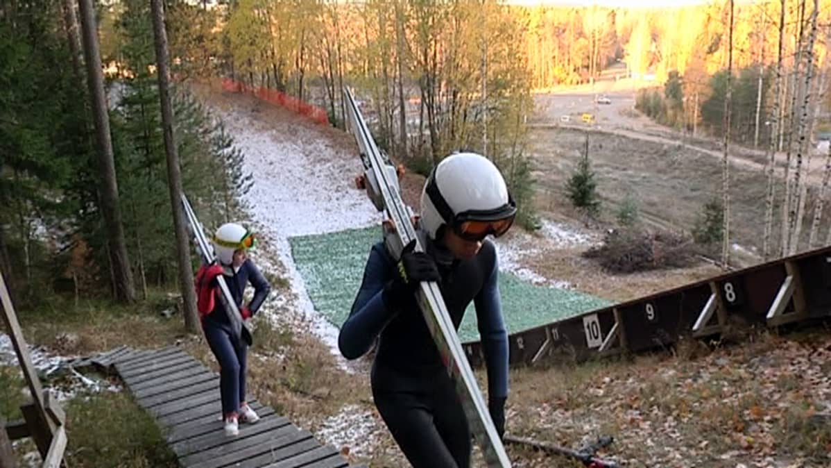 Kaksi mäkihyppääjää kiipeää hyppytorniin.