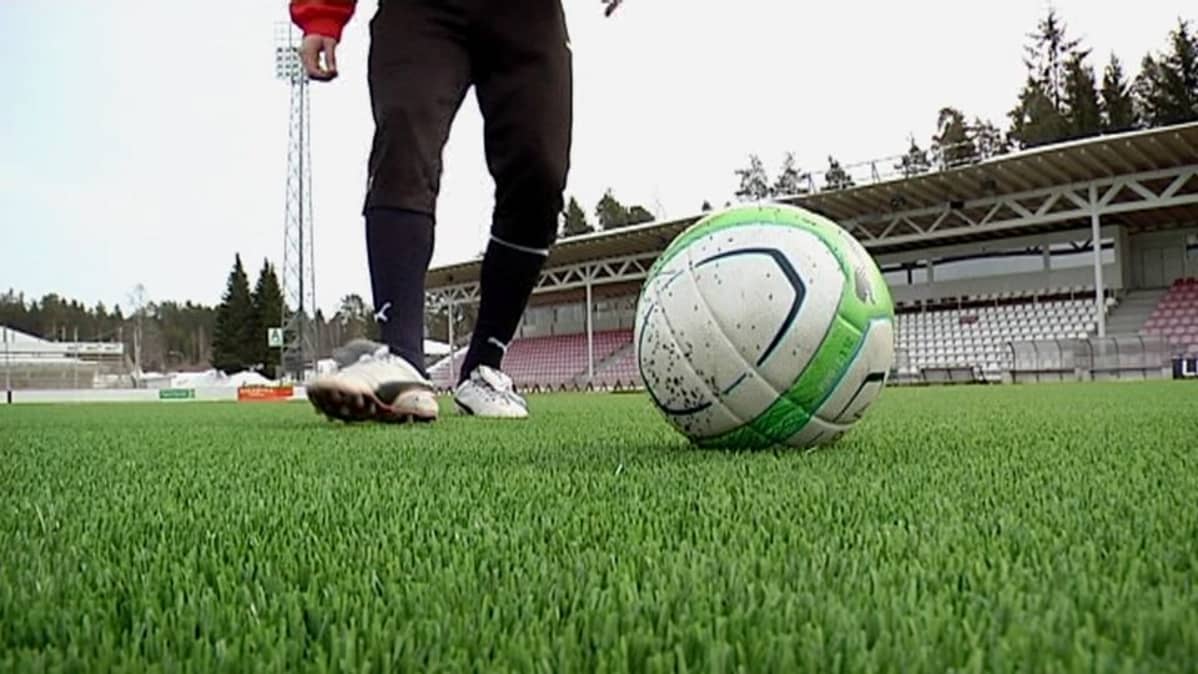 Jalkapalloilija ja pallo stadionin nurmella.