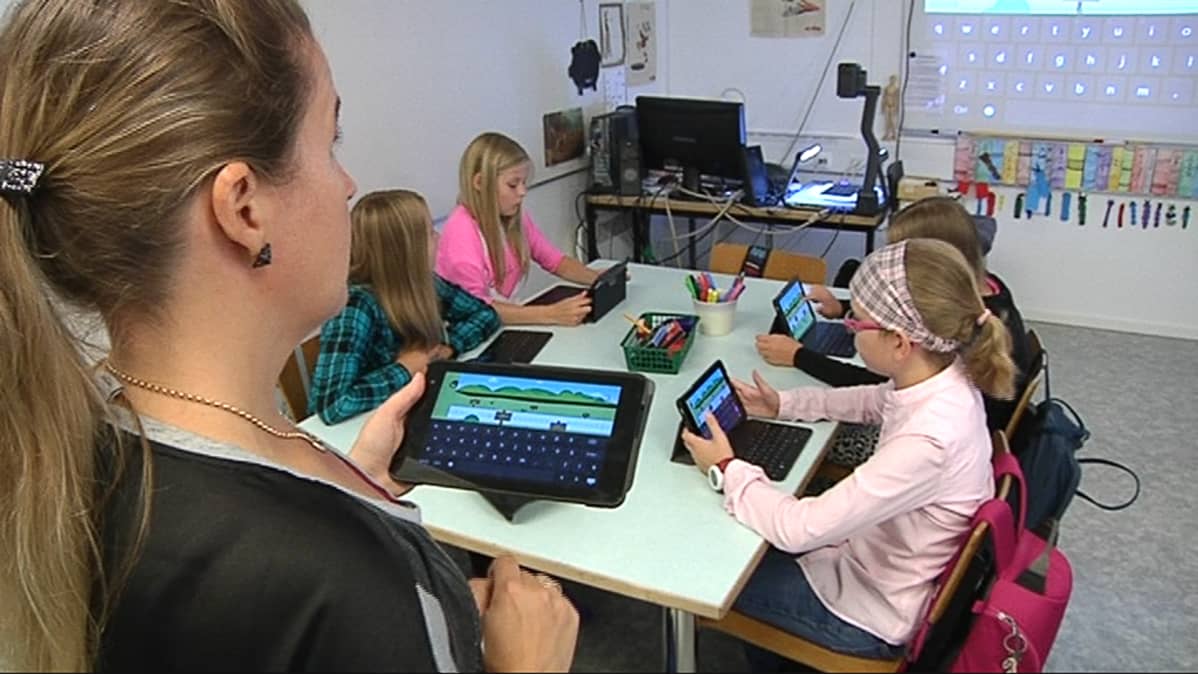 Kuvassa oppilaat ja opettaja tutkivat tabletti-tietokonetta.