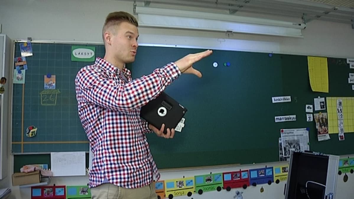 Luokanopettaja Timo Strickling seisoo luokan edessä iPad kädessään.