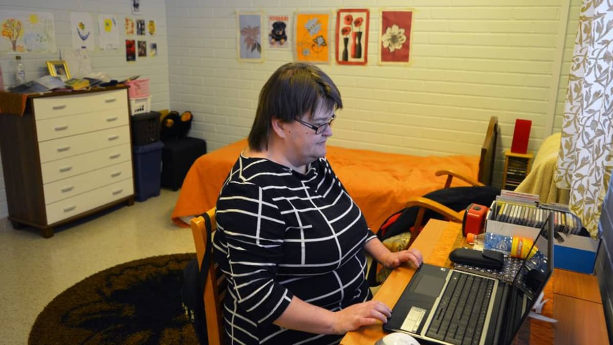 Mia Korhonen istuu palvelukeskuksessa omassa huoneessaan, pöydän ääressä tietokoneella.
