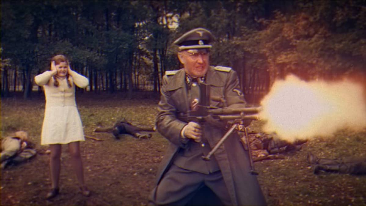 Konekiväärillä tulittava sotamies takanaan korviaan pitelevä hätäinen tyttö.