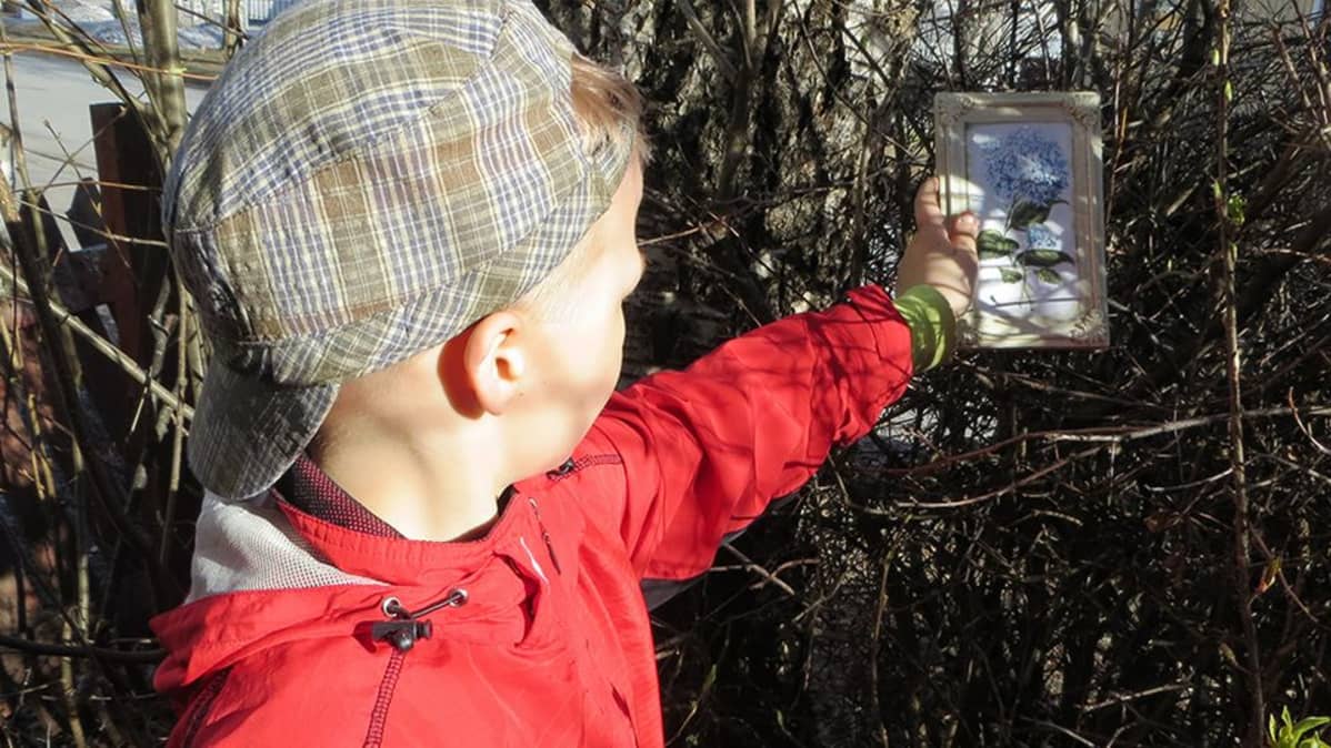 Pikkupoika asettelee taulua majan risuseinälle.