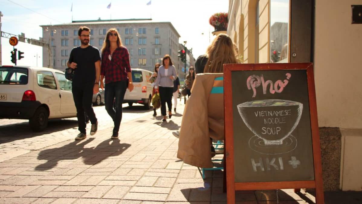 Ravintola HKI+:n kyltistä Unioninkadulla ja ohikäveleviä ihmisiä.