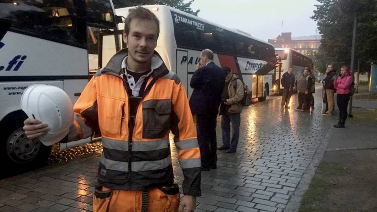 Työhaalariin pukeutunut mies seisoo mielenosoittajien bussien edessä Tampereen Keskustorilla.