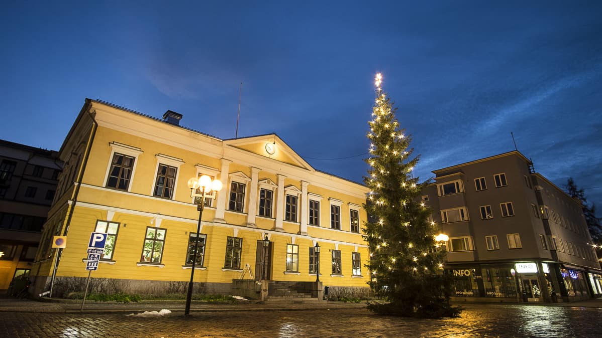 Joulukuusi Kokkolan Raatihuoneen edessä. Keltainnen rakennus, taustalla tummaa taivasta.