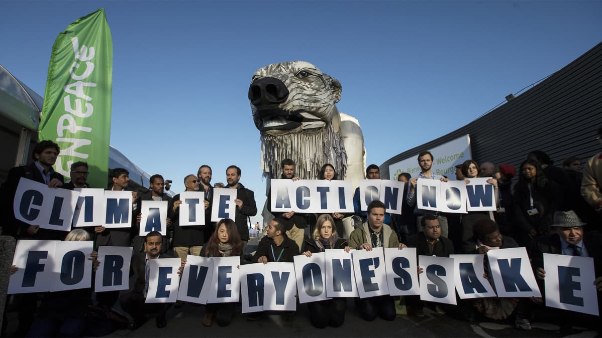 Reilu parikymmentä ihmistä pitelee käsissään kirjaimia joista muodostuu lause "climate action now for everyone's sake".