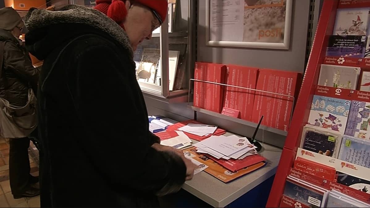 Nainen laittaa postimerkkiä joulukorttiin