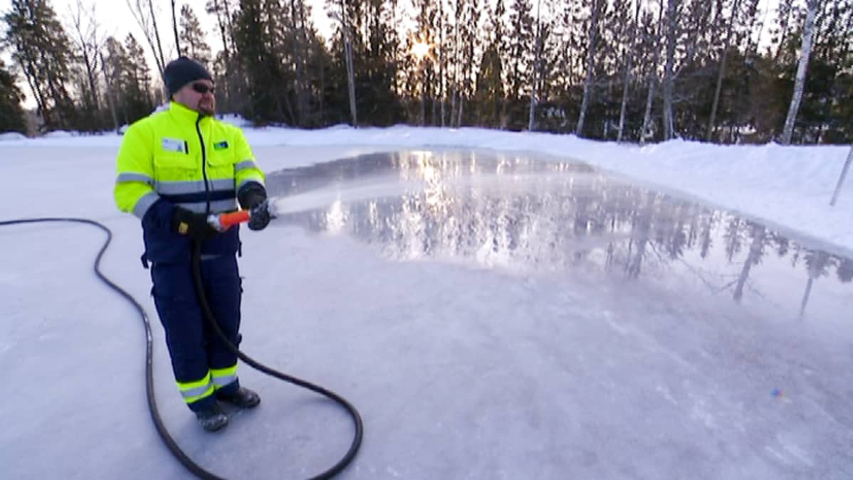 mies ruiskuttaa letkusta vettä luistinradalla