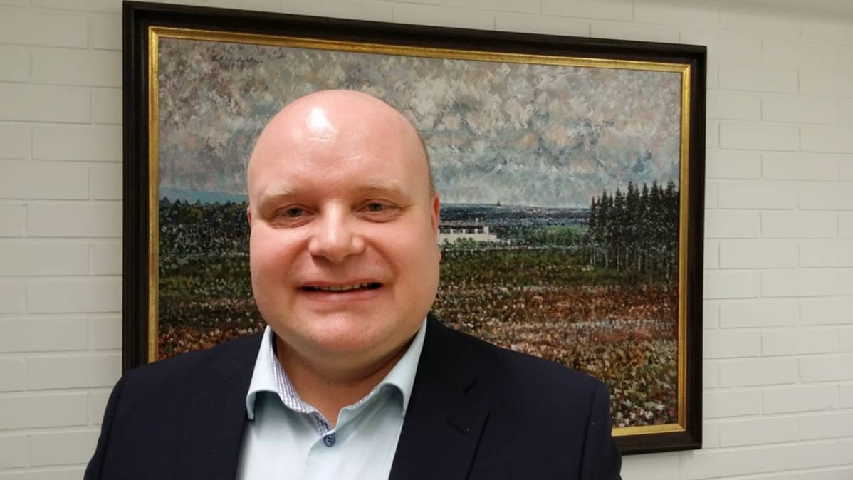 Toimitusjohtaja Juha Jokinen seisoo taulun edessä