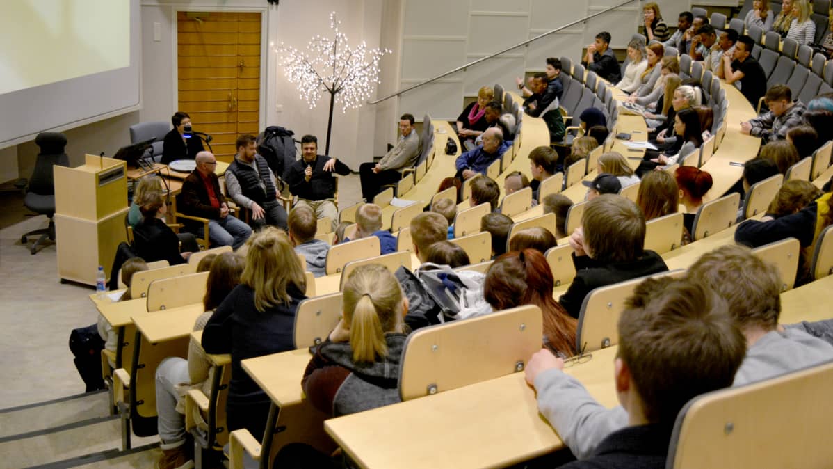 Lukiolaisista ja Kainuun opistolaisista koostuva yleisö seuraa uskontopaneelikeskustelua Kajaanin lukion auditoriossa.