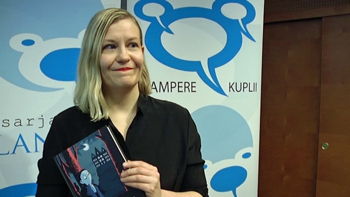 Kati Närhi seisoo palkitsemistilaisuudessa kirja kädessään.