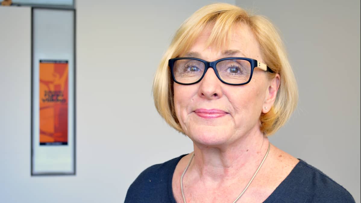 Runoviikon tapahtumapäällikkö Tuula Tikkanen seisoo runoviikko-julisteen edessä.
