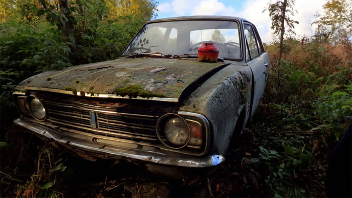 Hieman sammaloitunut auto pensaikossa, konepellillä kahvipannu.