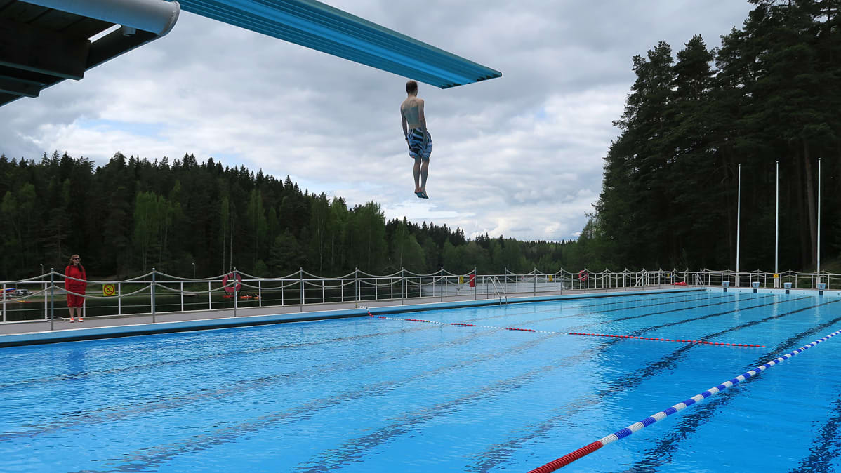 Mies hyppää hyppytornista altaaseen maauimalassa