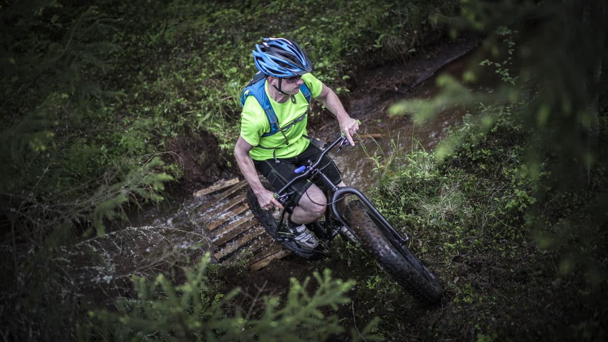 Kokkolalaisen pyöräilyseura Kammenkiertäjien fatbike-pyöräilijä ylittää puron.