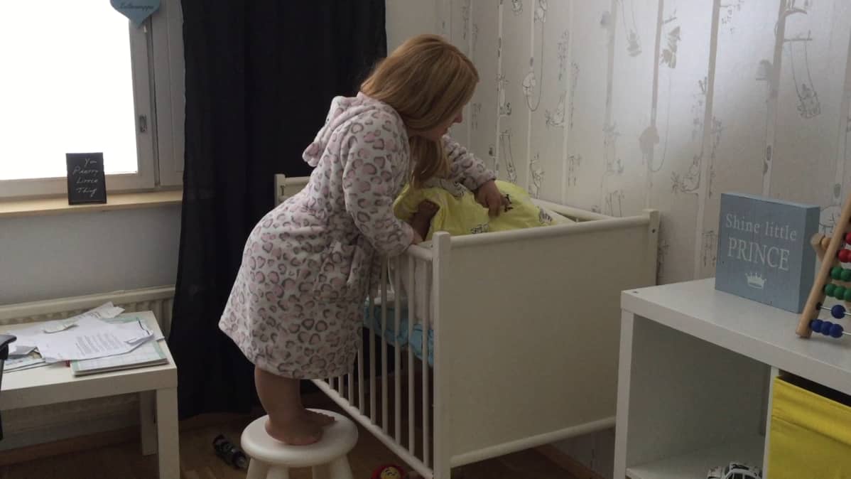 Milla Maria Lassila peittelee lasteen pinnasänkyyn.