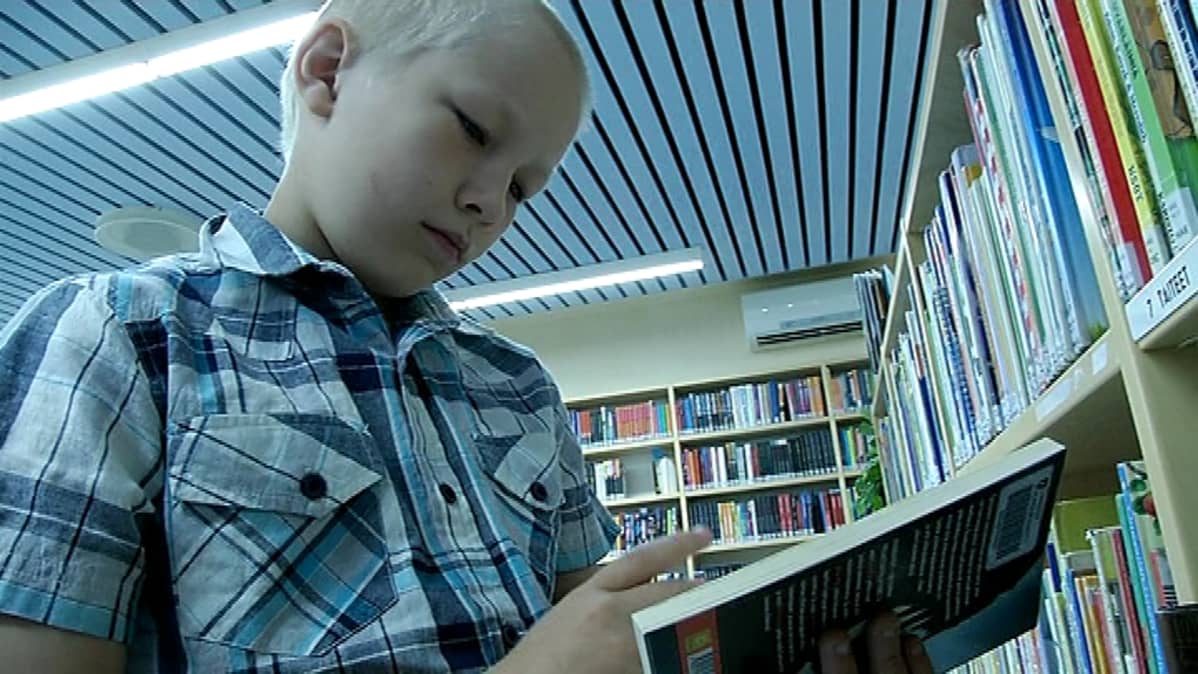 Poika katselee kirjaa kirjastossa