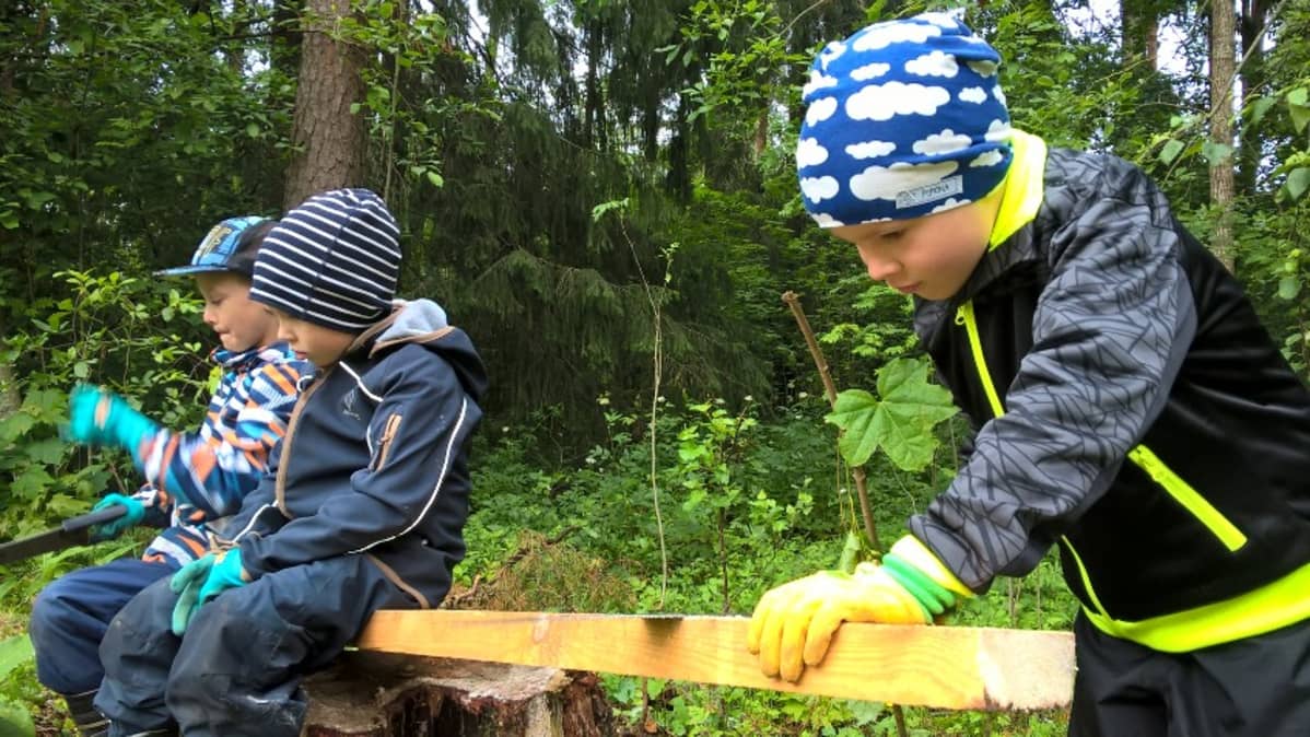 Henri Eilittä ja Eino Hirvilammi ovat lankunpainoina, kun Joonas Pajuranta sahaa majaan lego-pakettia.