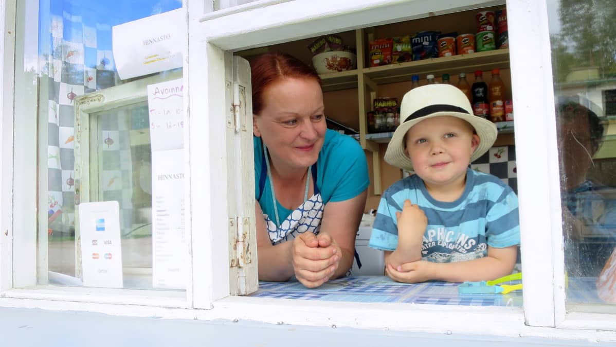 Lippalakkipäinen pikkupoikaja naismyyjä kioskin luukulla