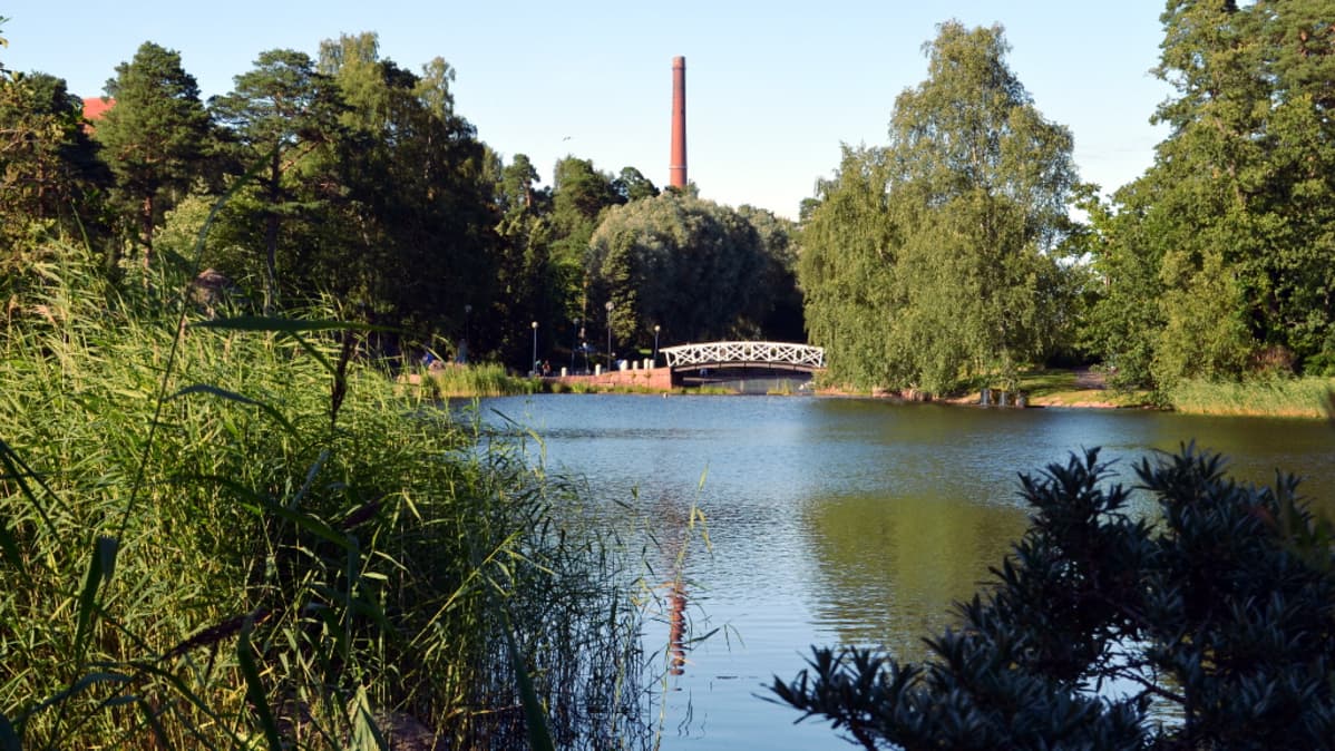 Koristeellinen kaarisilta ja teollisuuden savupiippu rinnakkain Kotkan Sapokan vesipuistossa.