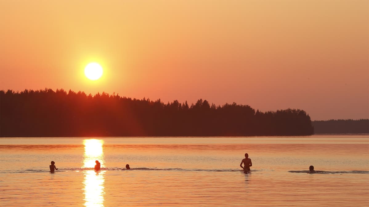 Ihmisiä uimassa järvessä auringonlaskun aikaan.