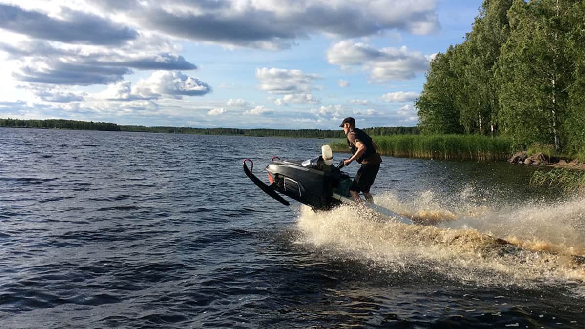 Moottorikelkkailija lähtee ajamaan järven rannasta, kelkan keula ilmassa.
