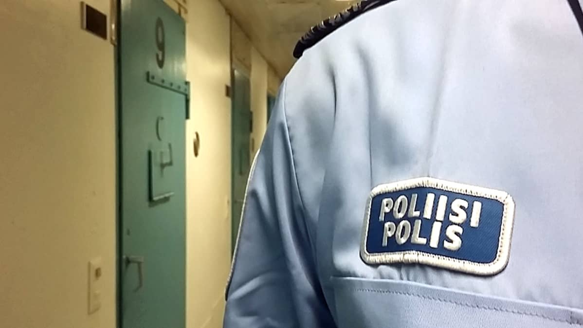 Poliisinmerkki virkapaidassa ja taustalla useita putkanovia.