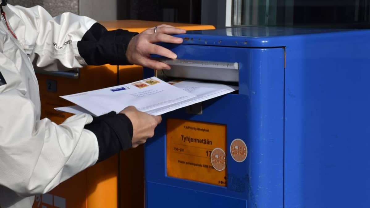 Nainen laittaa kirjeitä postilaatikkoon.
