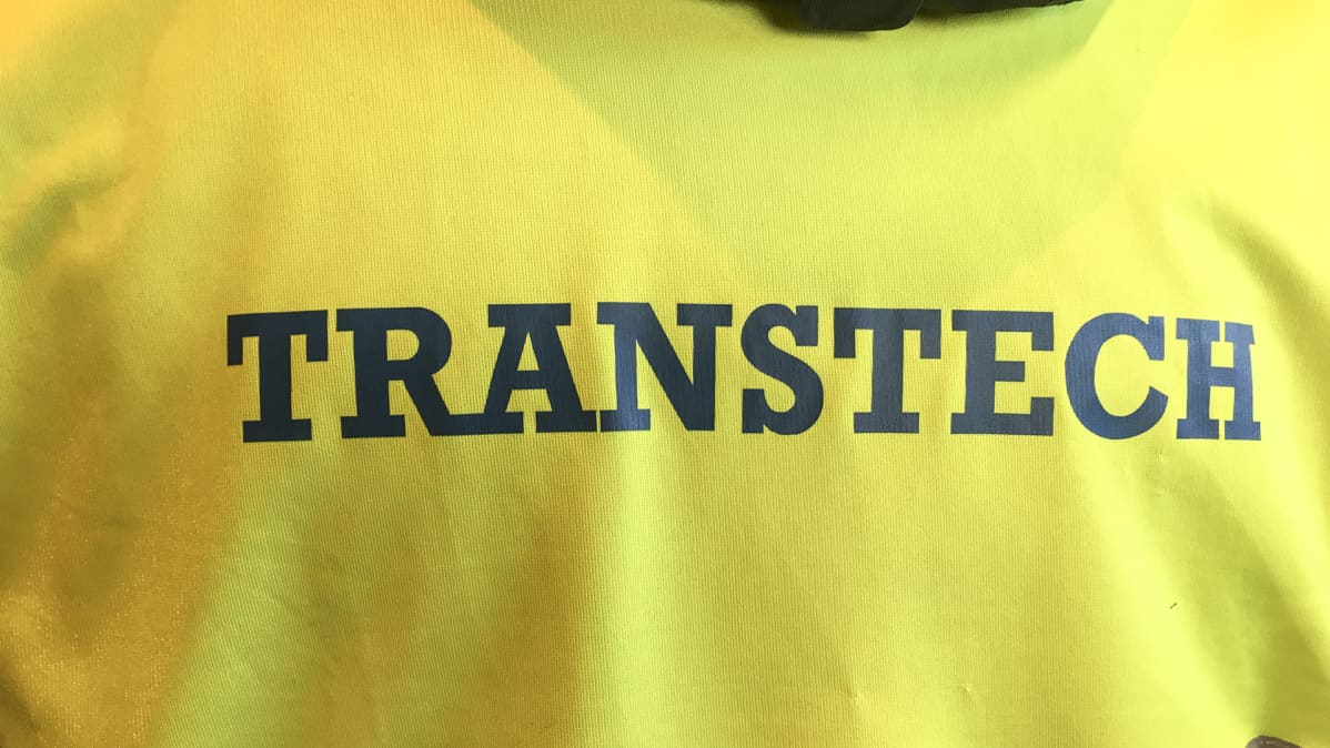 Teksti "Transtech" keltaisessa vaatteessa.