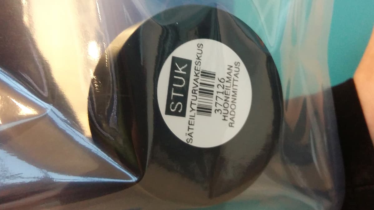 Musta radonmittauspurkki läpinäkyvässä muovipussissa