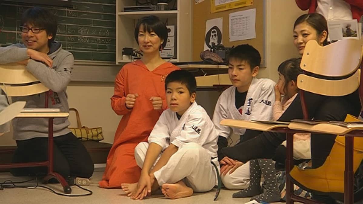 Japanilaisvieraat seuraavat kiinnostuneesti Veikkaalan koululaisten esityksiä.