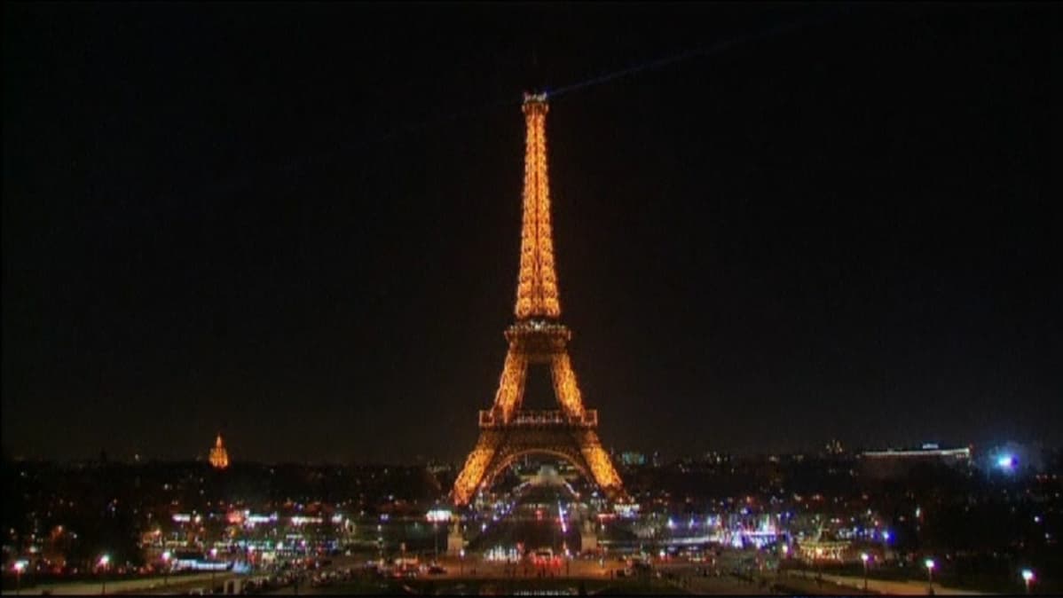 Pariisin Eiffel-torni loistaa pimeässä illassa, vielä valaistuna, hetkeä ennen valojen sammuttamista
