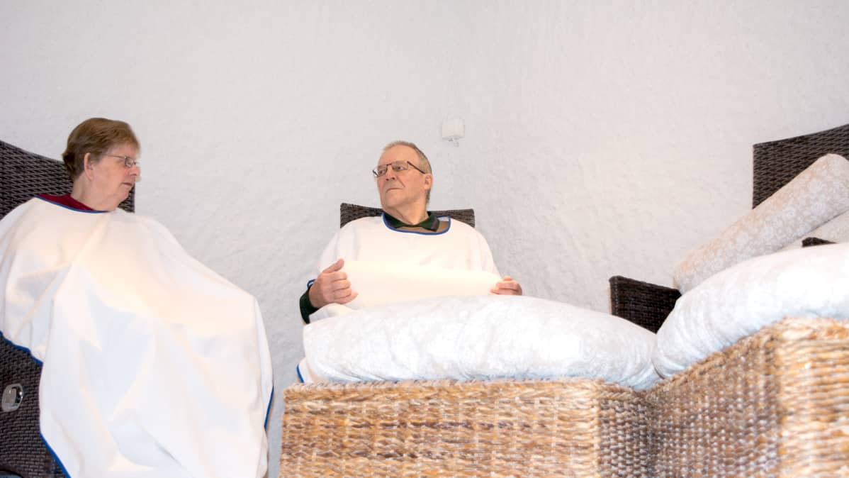 Pariskunta istuu suolahuoneessa suojakaavut yllä.