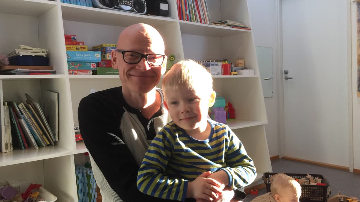 Tyytyväinen poika istuu hymyilevän isänsä sylissä.