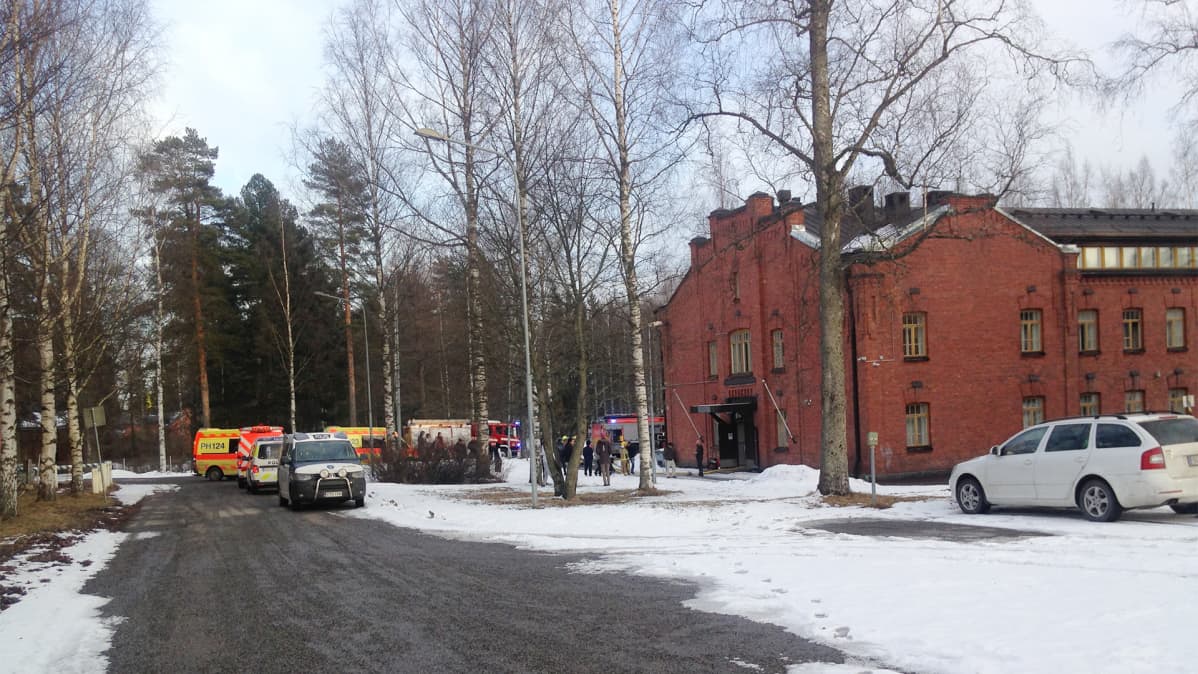 Hälytysajoneuvoja punatiilisen rakennuksen ulkopuolella.