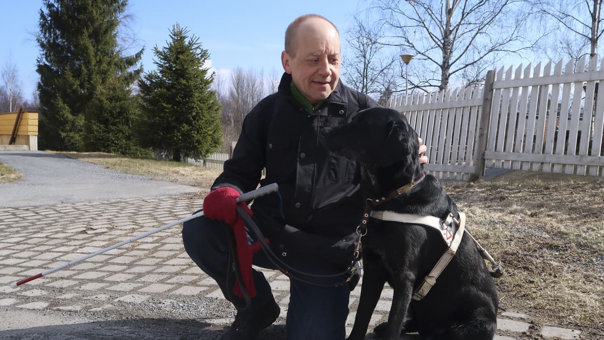 Janne Silas kyykistyneenä silittämään opaskoiraansa Uunoa.