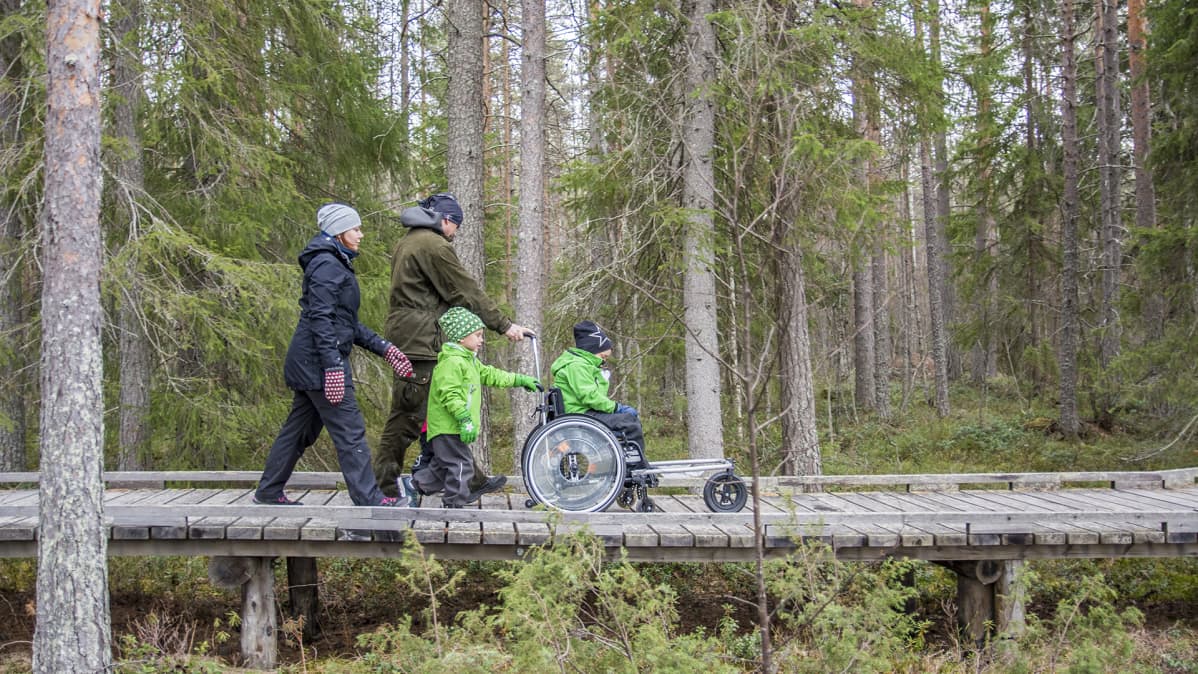 Kähköset kulkevat luonnossa pyörätuolin kanssa.
